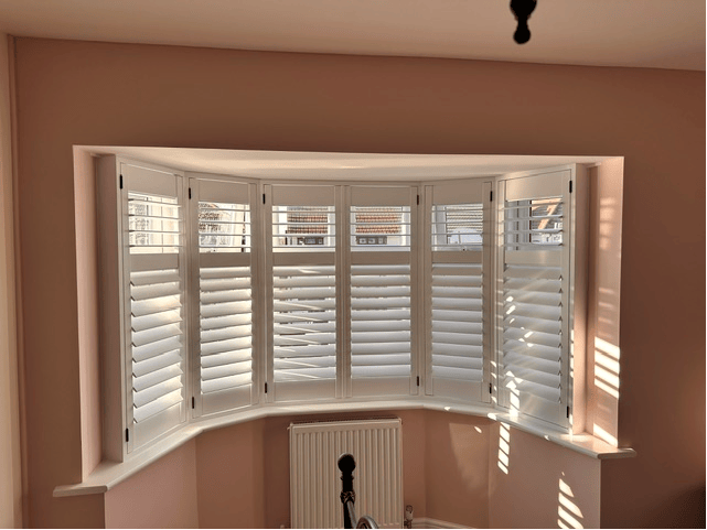 Curved bay shutters in a soft pink room